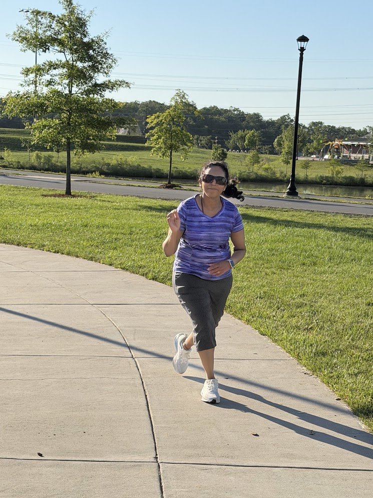 A runner in sunglasses on a paved path beside a park