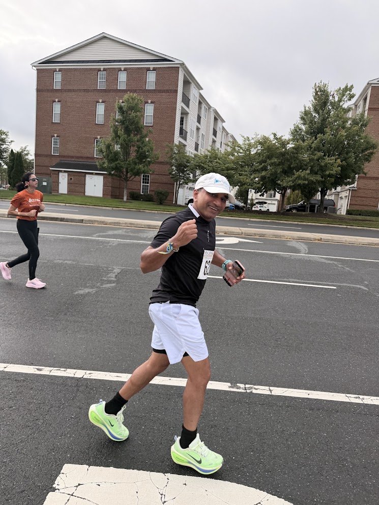 A runner with a race bib on a city street, another runner behind
