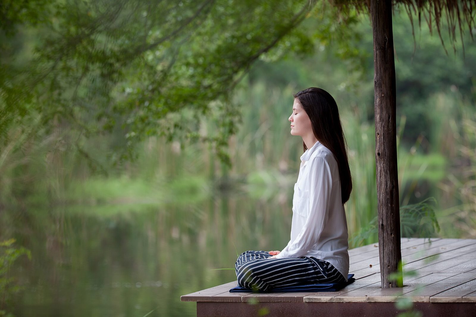 A person sitting cross-legged on a wooden deck beside a quiet river