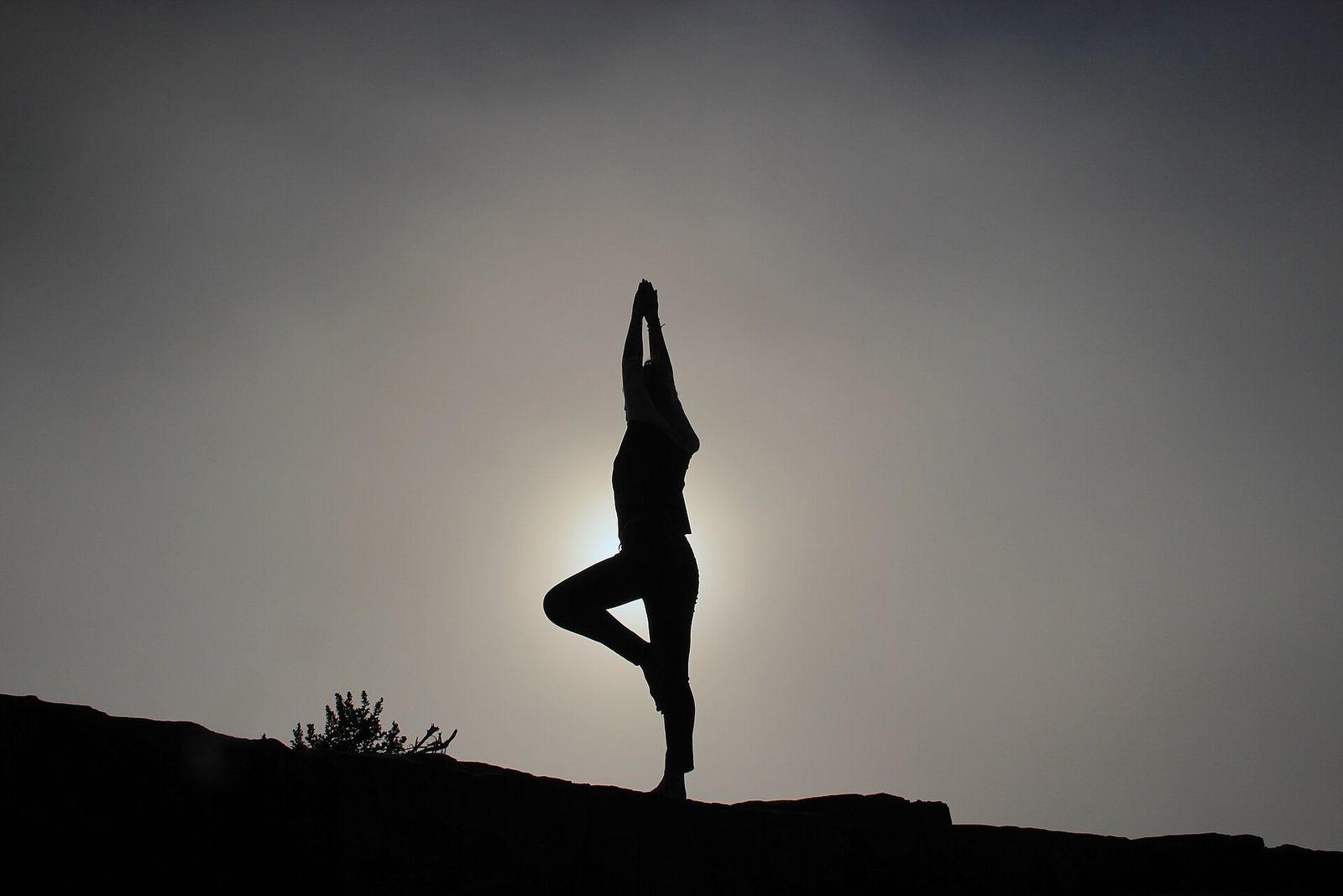 A person in tree pose silhouetted against the sun on a ridge